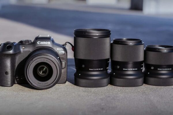 Об'єктив Sigma 16mm f/1.4 DC DN Contemporary поруч із лінійкою фіксів 30mm і 56mm на фоні камери Canon EOS R7
