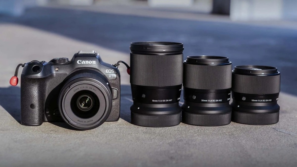 Об'єктив Sigma 16mm f/1.4 DC DN Contemporary поруч із лінійкою фіксів 30mm і 56mm на фоні камери Canon EOS R7