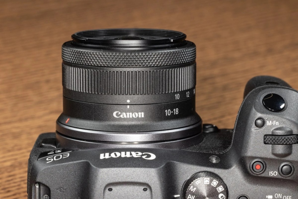 Об'єктив Canon RF-S 10-18mm f/4.5-6.3 IS STM на байонеті камери Canon EOS R7: вид згори на байонетне з'єднання та верхню панель камери з кнопкою M-Fn і диском ISO на дерев'яному столі